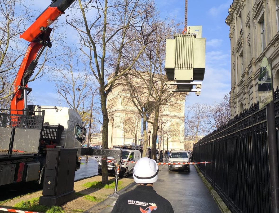 Transformateur hissé par une grue dans une rue de Paris, sous la conduite d’un technicien