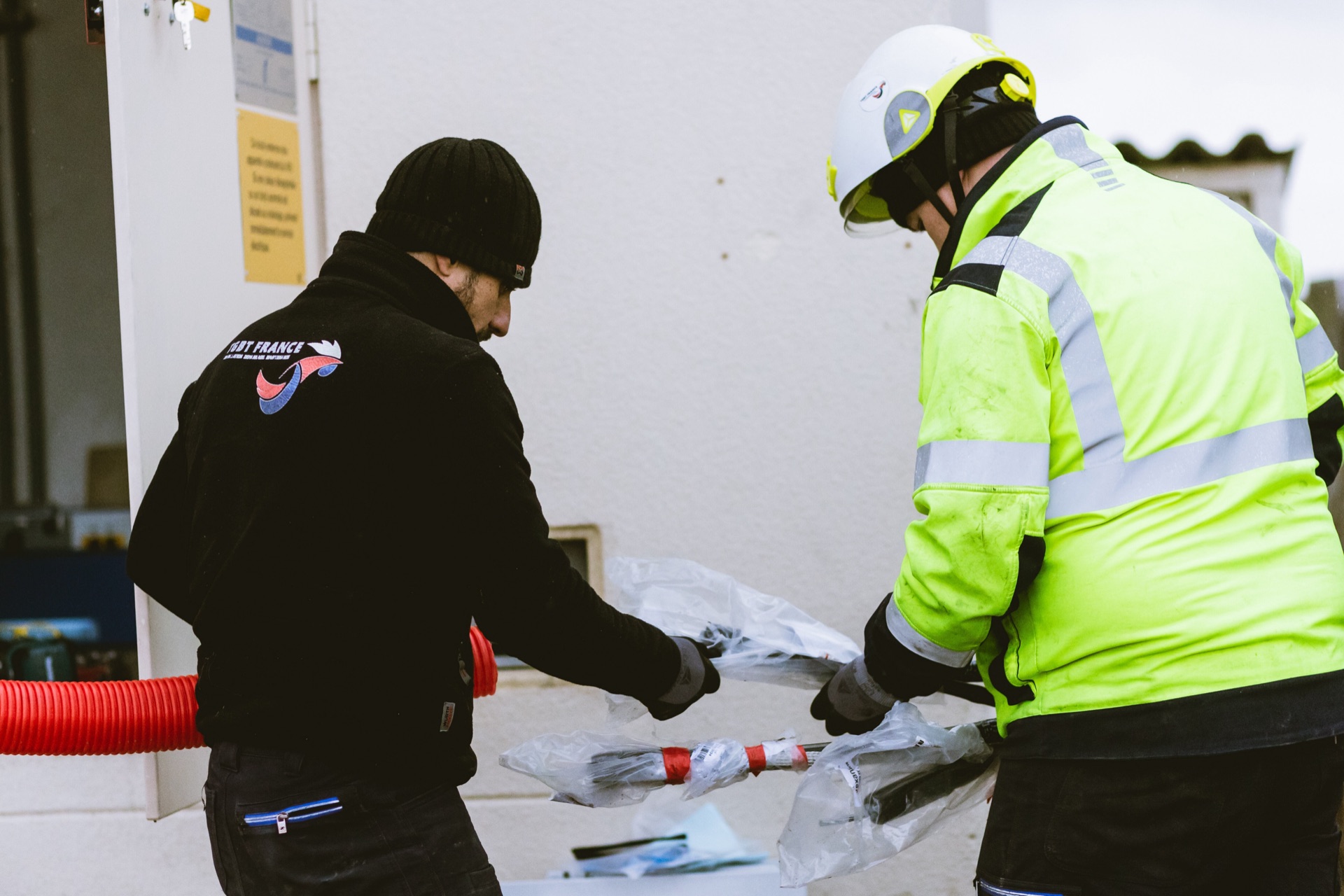Deux techniciens, dont l’un en tenue haute visibilité, préparent des câbles haute tension au pied d’un poste électrique